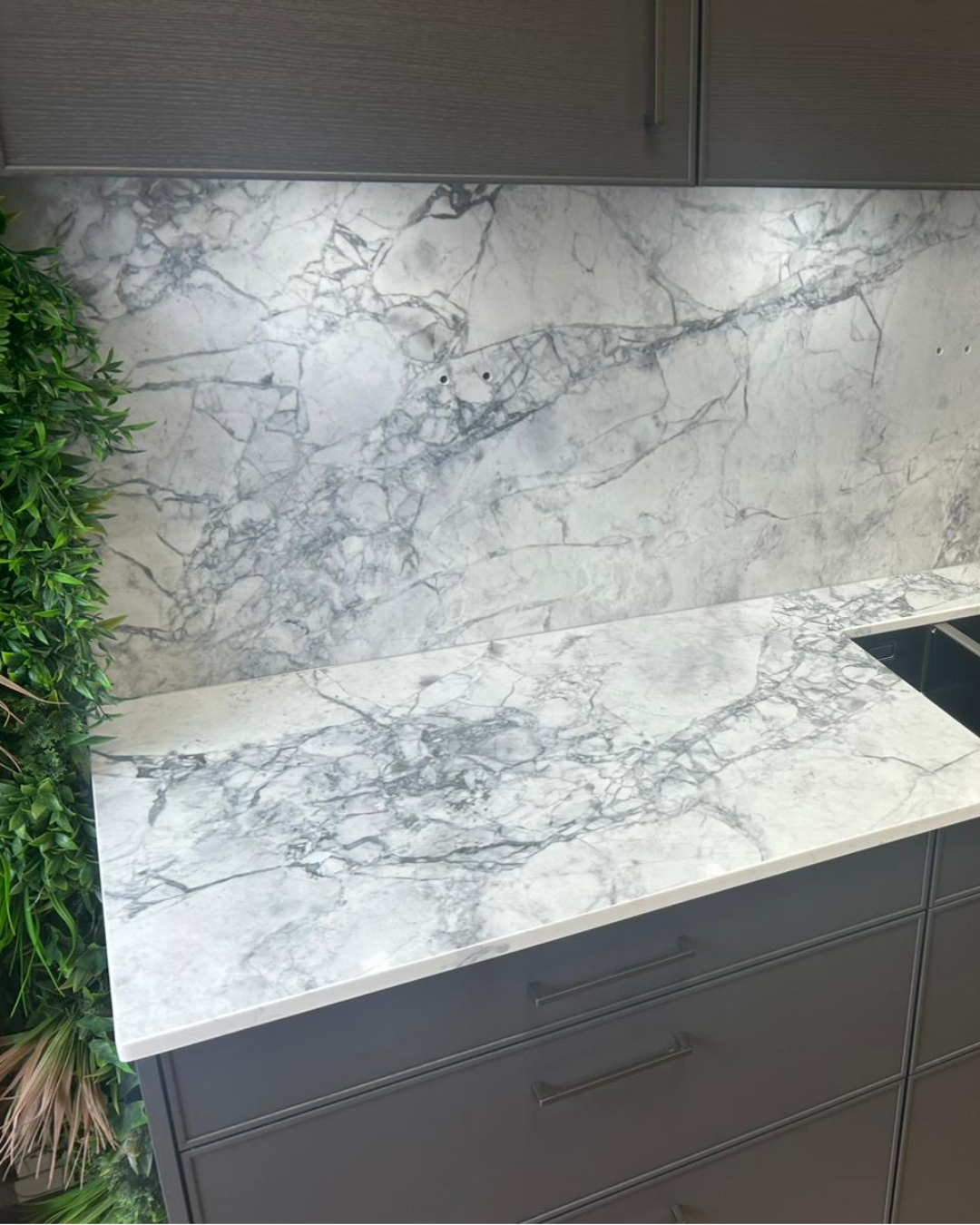 Marble-patterned Eclipsia quartz kitchen countertop with grey cabinets and greenery on the side.
