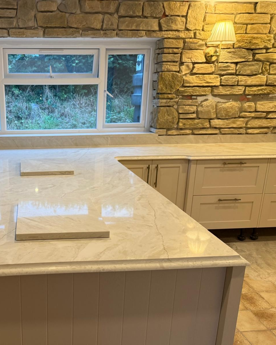 Kitchen with stone wall, window, and taj mahal quartz worktops with ogee edge