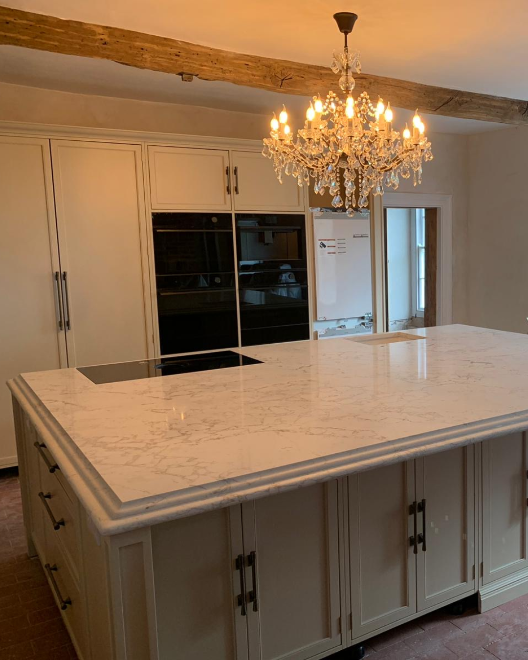 Modern kitchen with Arabescato Cremo Lydia quartz island and chandelier