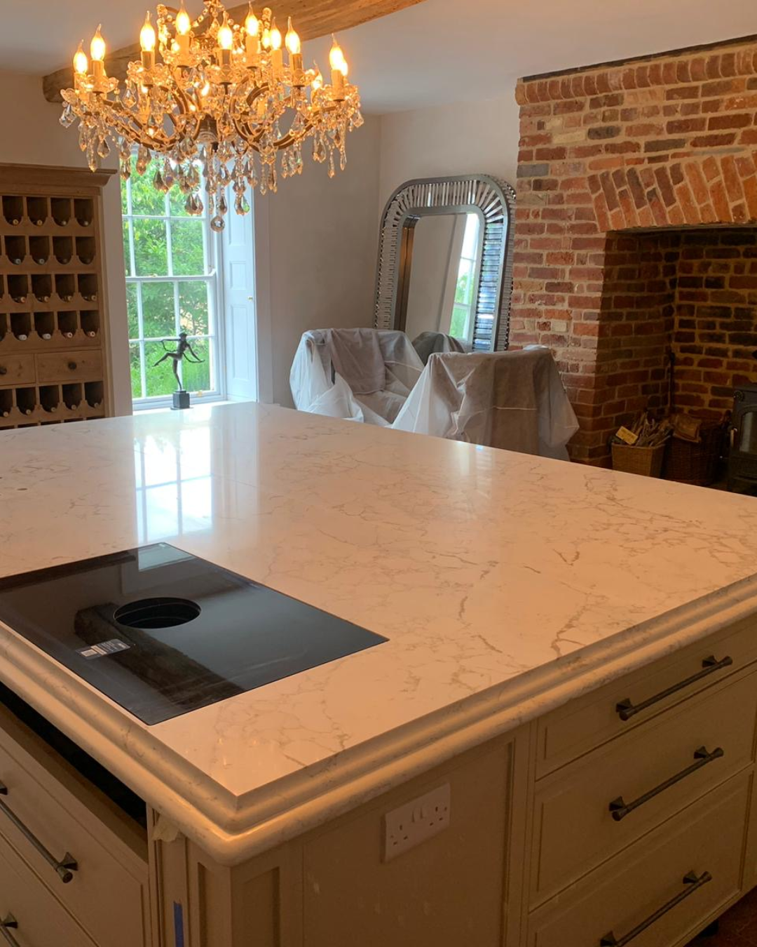 Arabescato Cremo Lydia Quartz kitchen island with chandelier and brick wall in background
