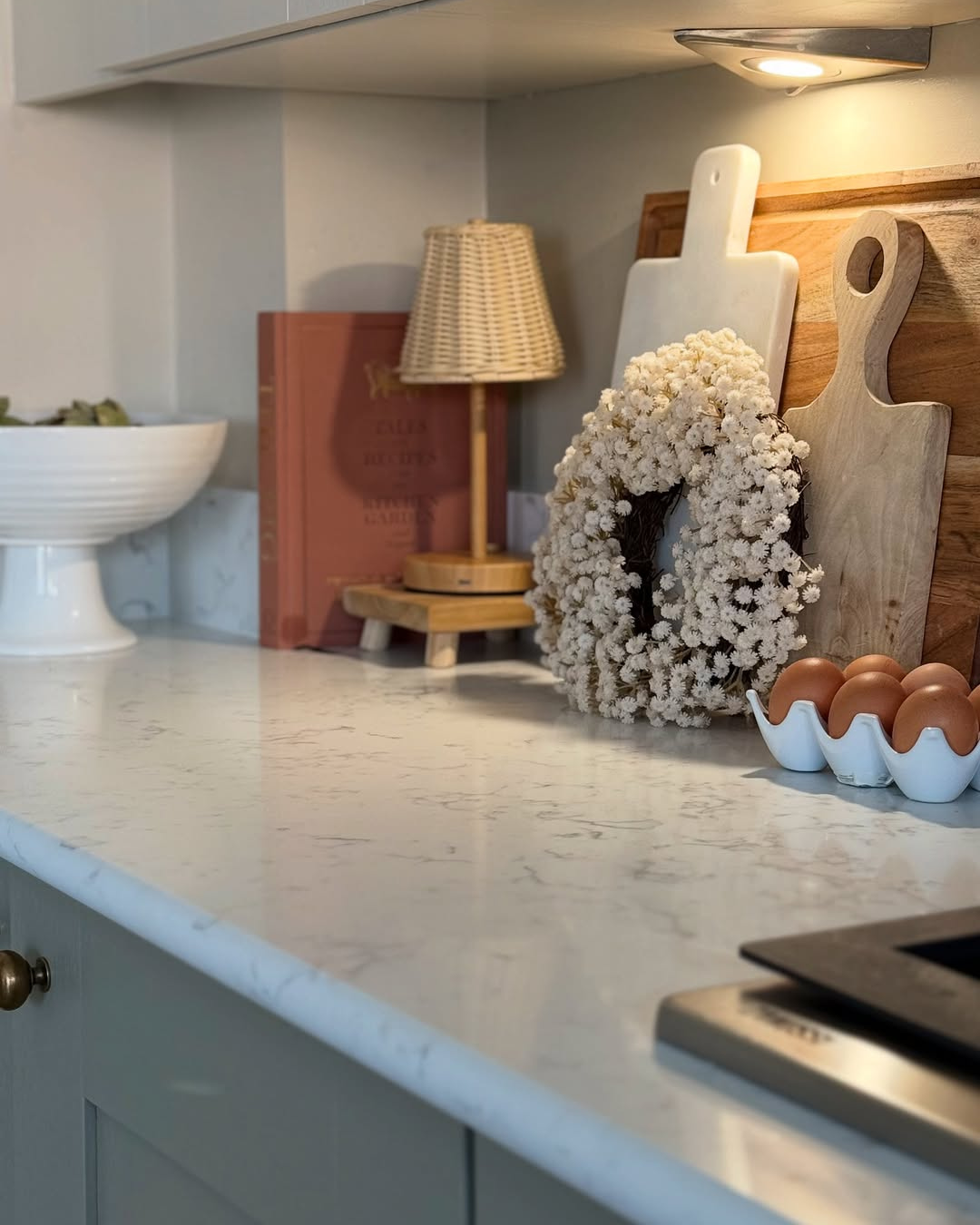Kitchen counter with carrara white quartz surface, decorative wreath, cutting board, and egg carton.