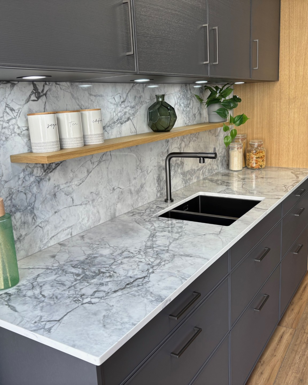 Modern kitchen with grey cabinets, Eclipsia quartz worktop, and wooden shelves.