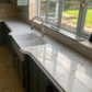Kitchen with royal oro quartz countertop and sink, large window showing garden view.