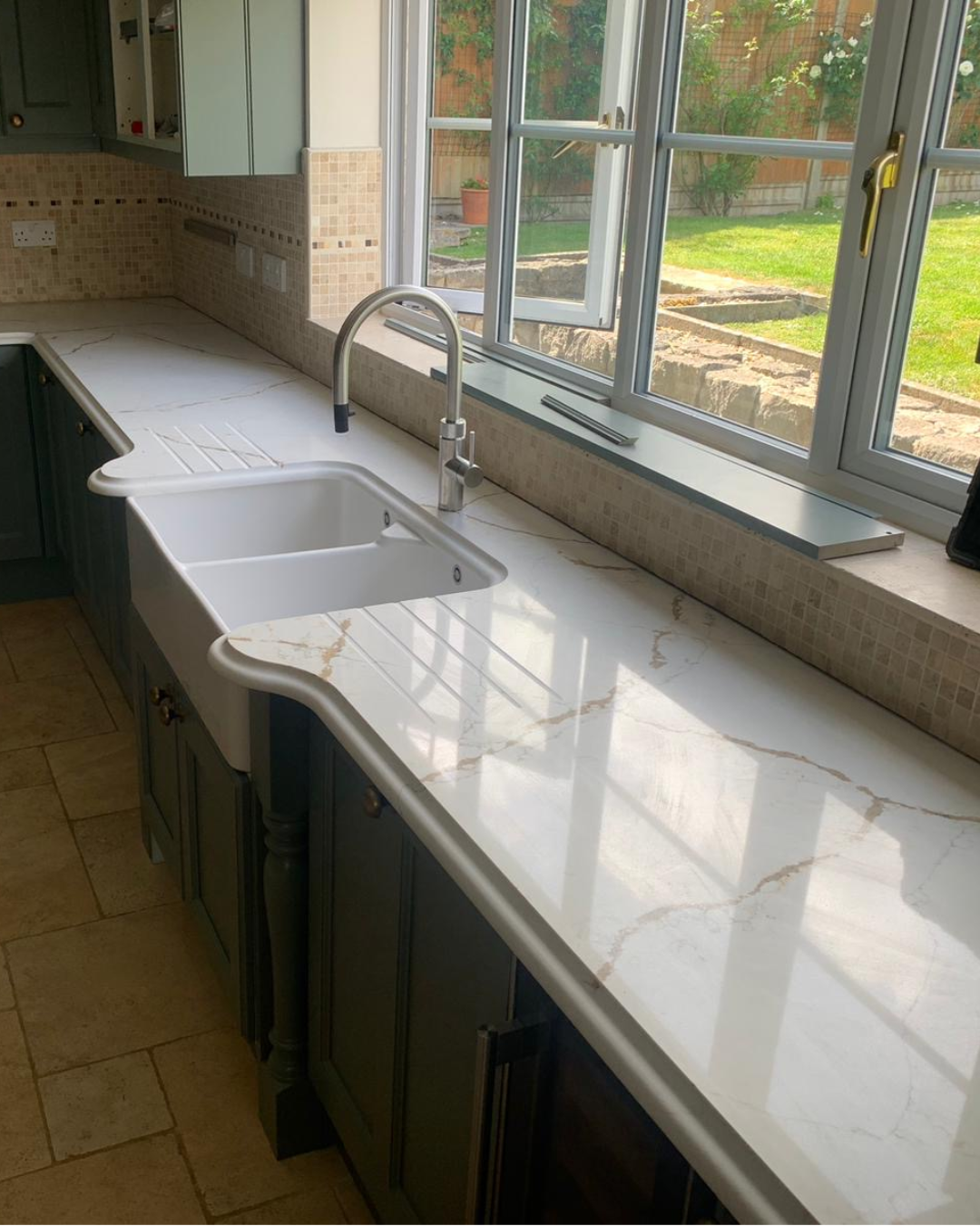 Kitchen with royal oro quartz countertop and sink, large window showing garden view.